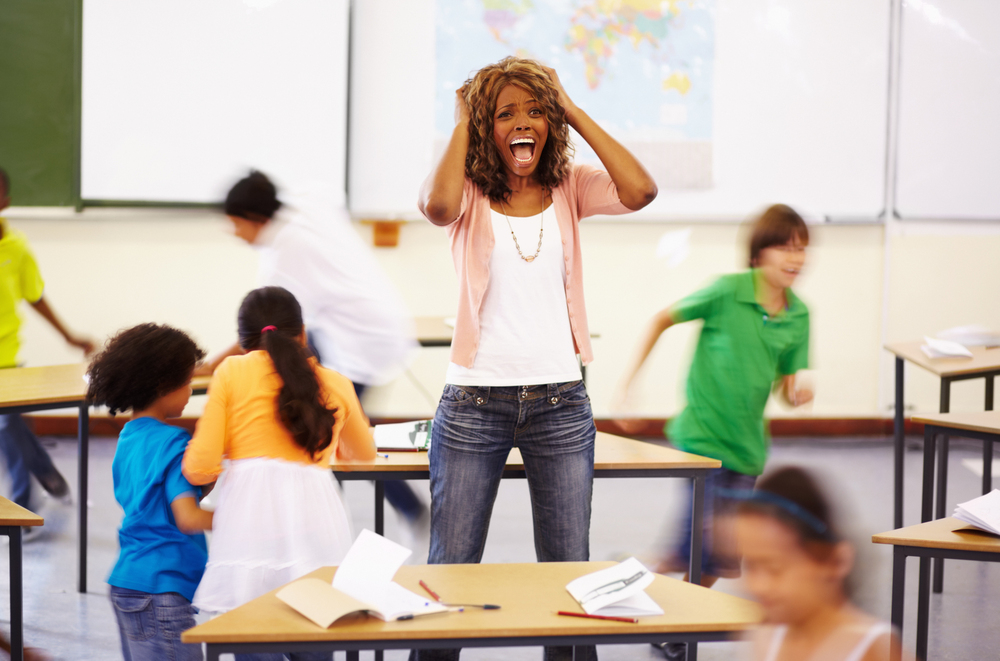 Kids create chaos. A young teacher screaming as children run around the classroom